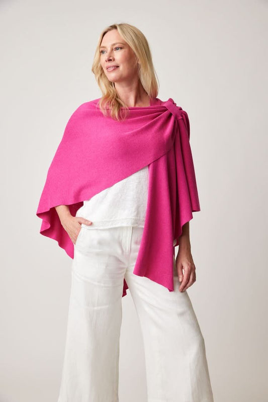 A woman wearing white top and pants drapes the bright pink, cotton-rich Parkhurst Covi Wrap over her shoulder against a plain background.