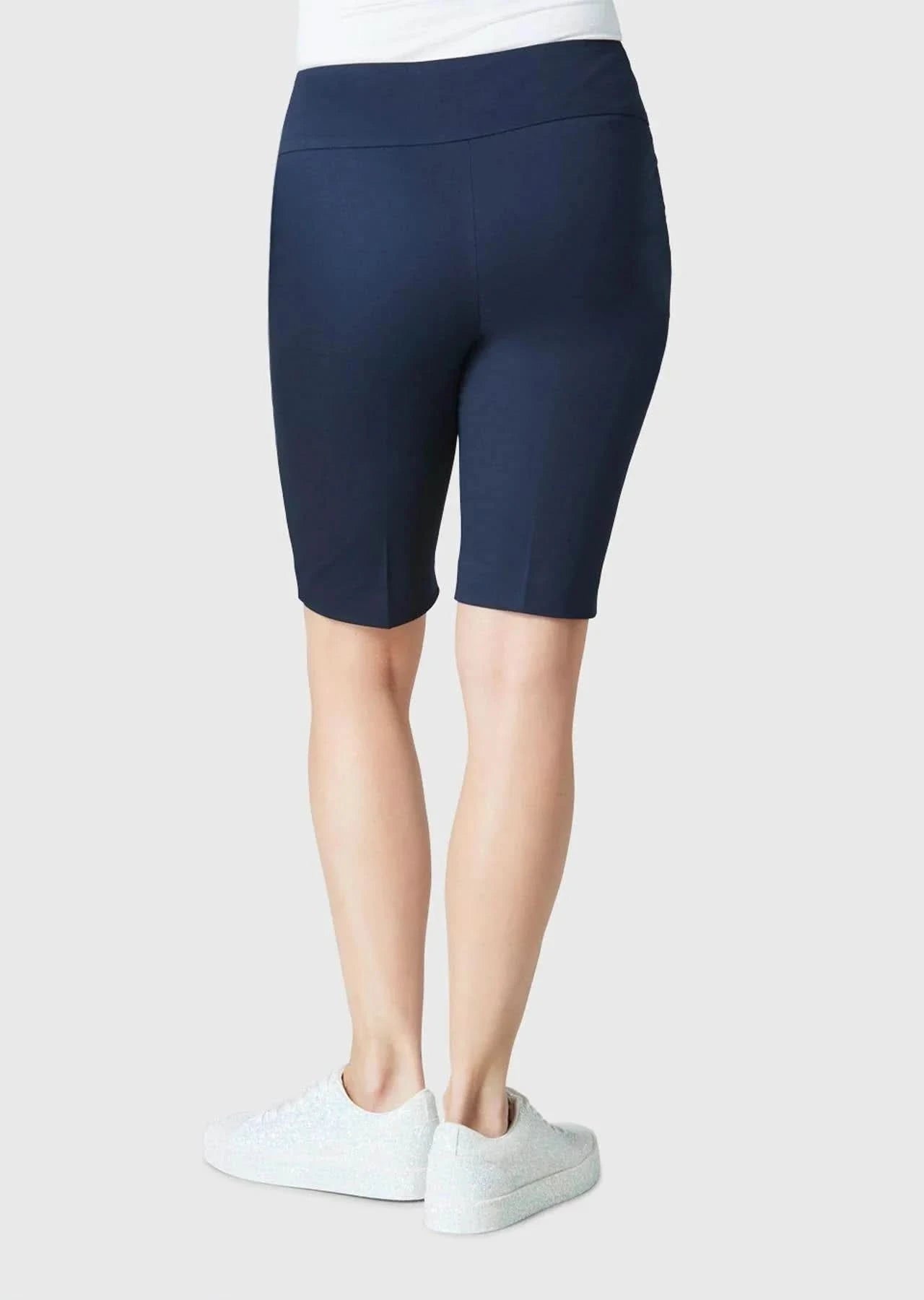 A person is seen from behind wearing Lisette’s navy Streach Bermuda Short, white sneakers, and a white top against a plain background—an ideal warm-weather outfit.