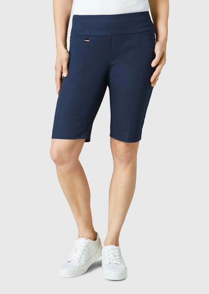 A person is seen from behind wearing Lisette’s navy Streach Bermuda Short, white sneakers, and a white top against a plain background—an ideal warm-weather outfit.