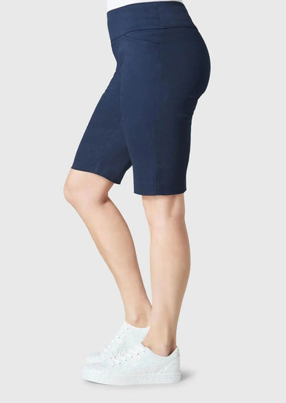 A person is seen from behind wearing Lisette’s navy Streach Bermuda Short, white sneakers, and a white top against a plain background—an ideal warm-weather outfit.