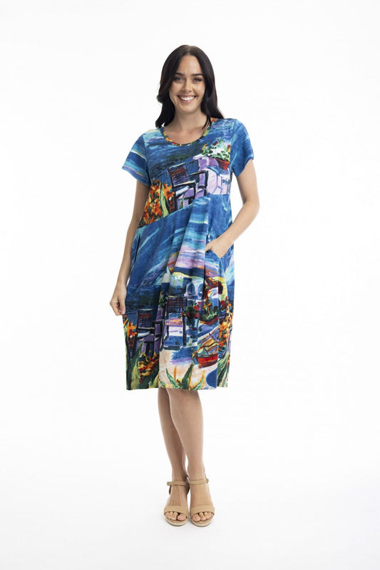 A woman wears the Orientique Cotton Short Sleeve Bubble Dress, featuring a colorful abstract print, styled with tan heeled sandals, standing against a white background.