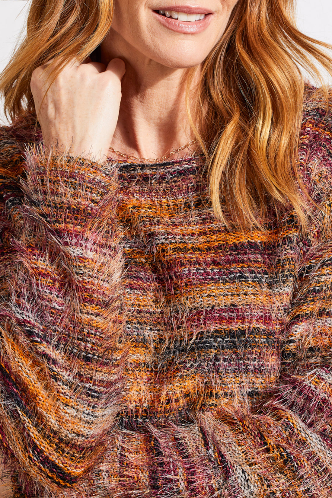 A person wearing a vibrant Tribal Soft Luxe Eyelash Long Sleeve Sweater in shades of orange, purple, and brown gently touches their hair.