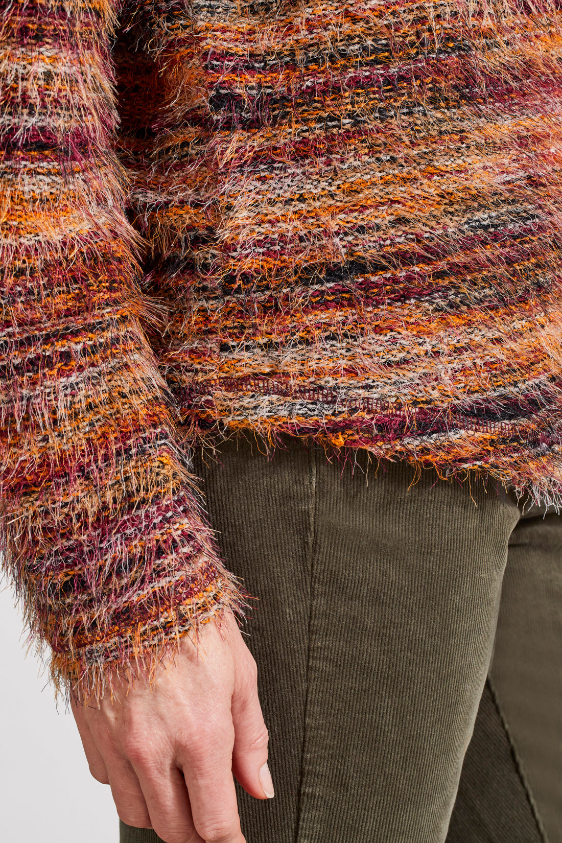 A person wearing a vibrant Tribal Soft Luxe Eyelash Long Sleeve Sweater in shades of orange, purple, and brown gently touches their hair.