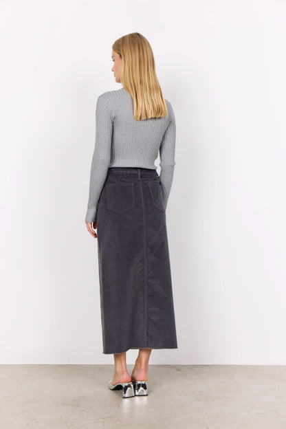 Person wearing a gray corduroy Soya Concepts IVALOU 2 Long Skirt with a front slit and a gray long-sleeve top, standing on a concrete floor in silver open-toe heeled sandals, exuding effortless style.