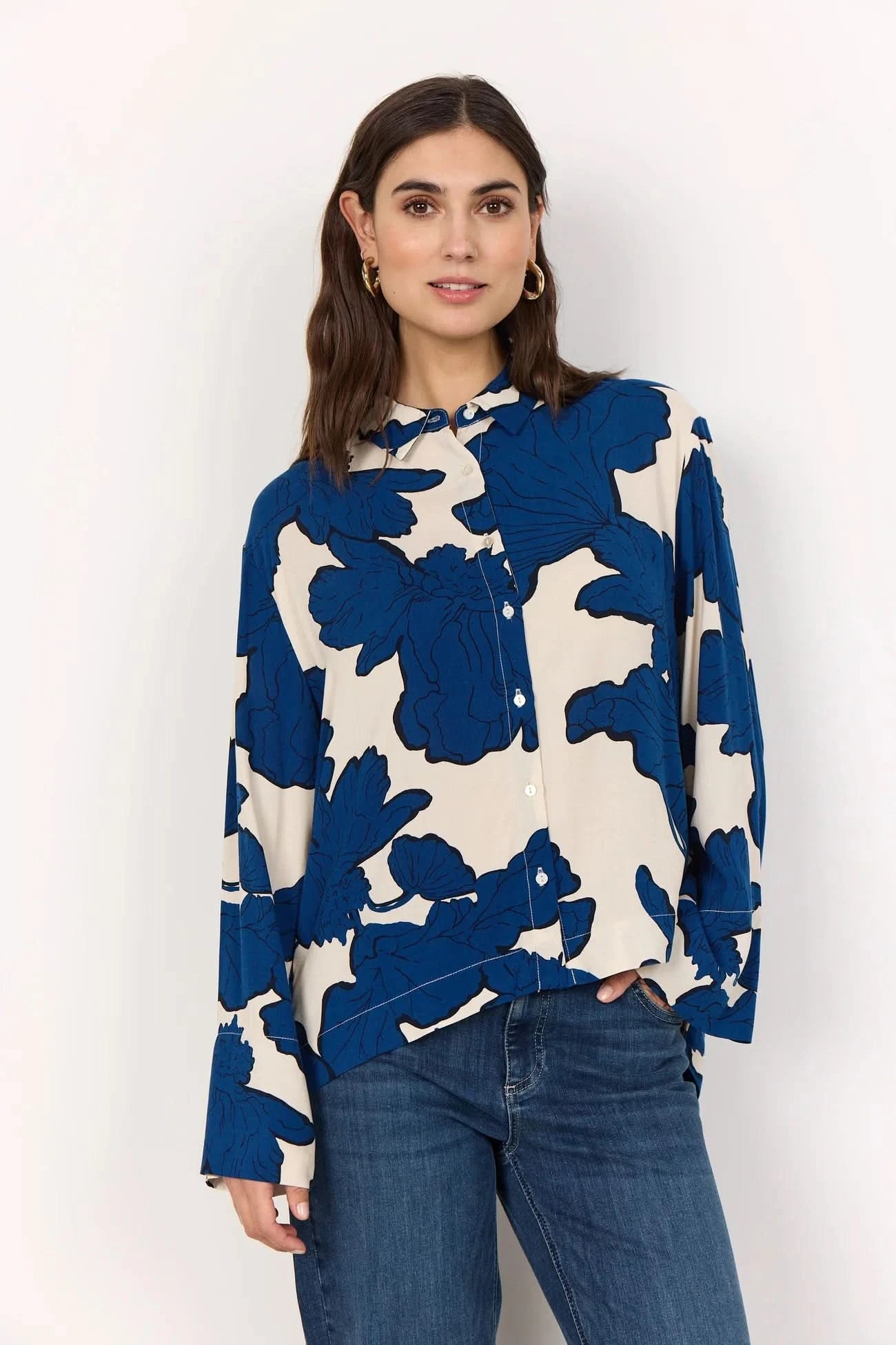 A woman wears the BLUE FLORAL PRINT BLOUSE by Soya Concepts, crafted from Ecovero viscose with bold blue abstract floral patterns, paired with blue jeans against a plain light background.