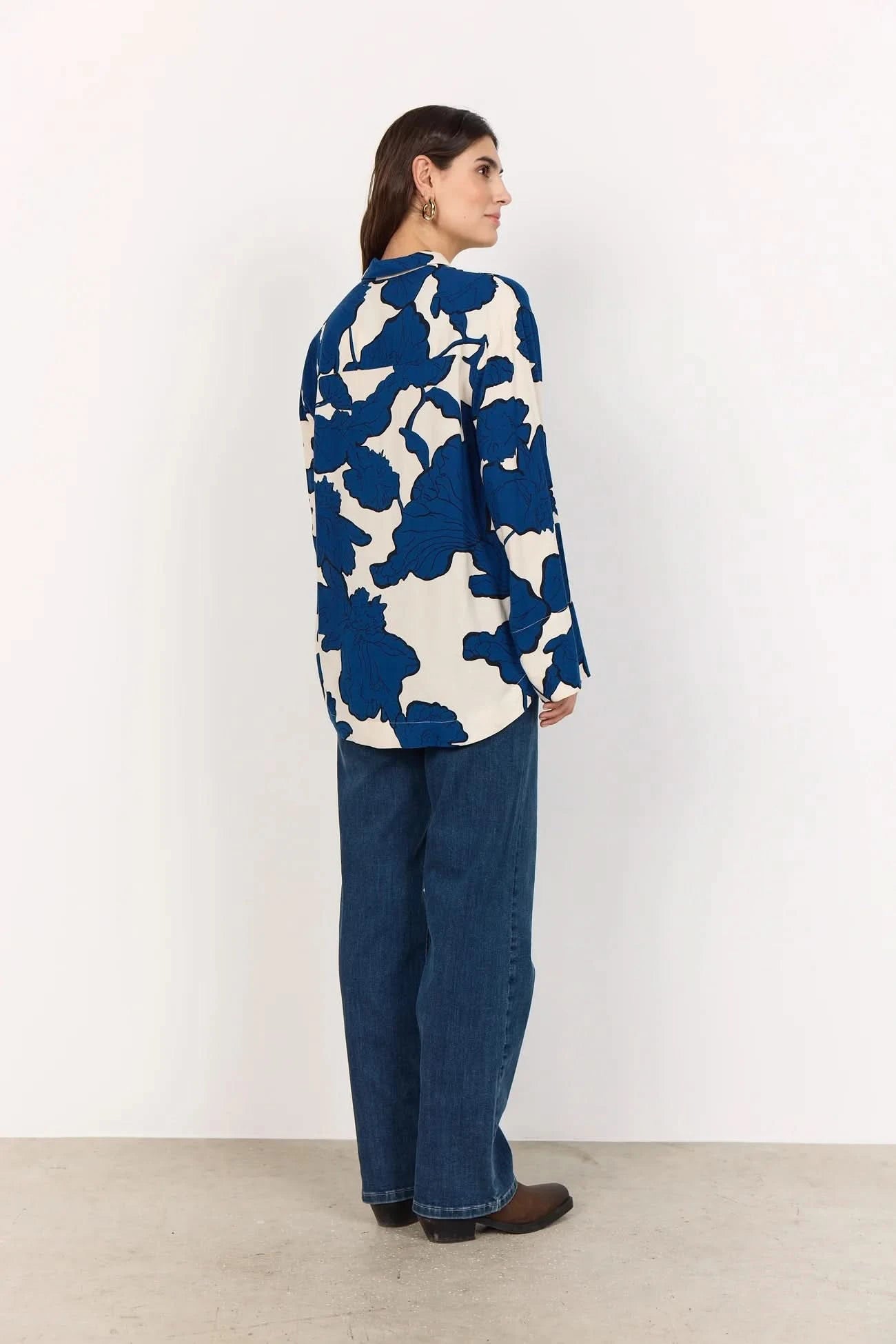 A woman wears the BLUE FLORAL PRINT BLOUSE by Soya Concepts, crafted from Ecovero viscose with bold blue abstract floral patterns, paired with blue jeans against a plain light background.