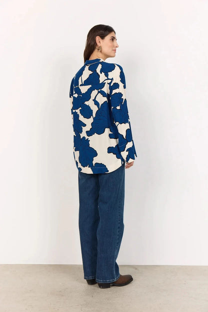 A woman wears the BLUE FLORAL PRINT BLOUSE by Soya Concepts, crafted from Ecovero viscose with bold blue abstract floral patterns, paired with blue jeans against a plain light background.
