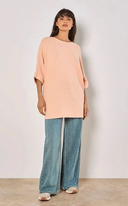 A person in a versatile Apricot Batwing Waffle Knit Top and blue jeans poses against a plain background, with one hand in their pocket.