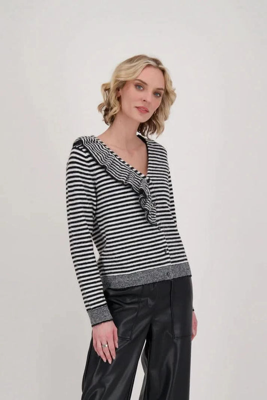 A woman dressed in a Gabby Isabella Ruffle Neck Stripe Sweater Top with black and white accents and black leather pants stands against a plain background.
