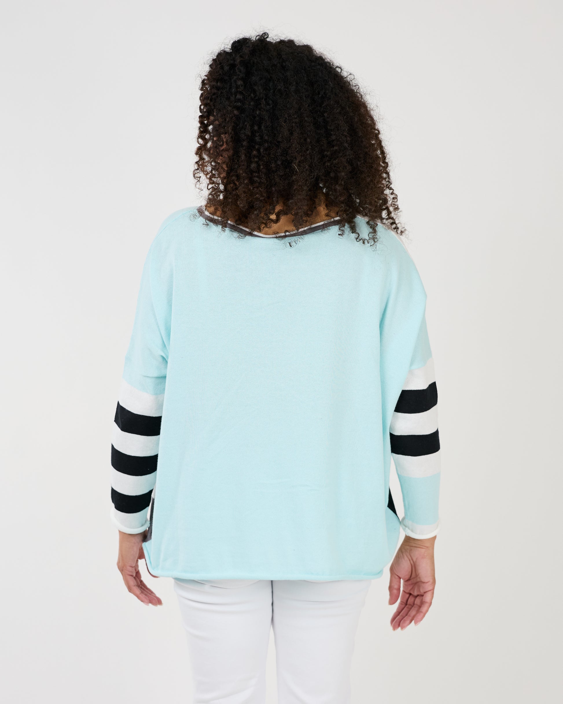 Woman smiling at the camera while playfully gesturing with her hand on her shoulder, wearing a Shannon Passero Lyara Longsleeve Crew Neck Top.