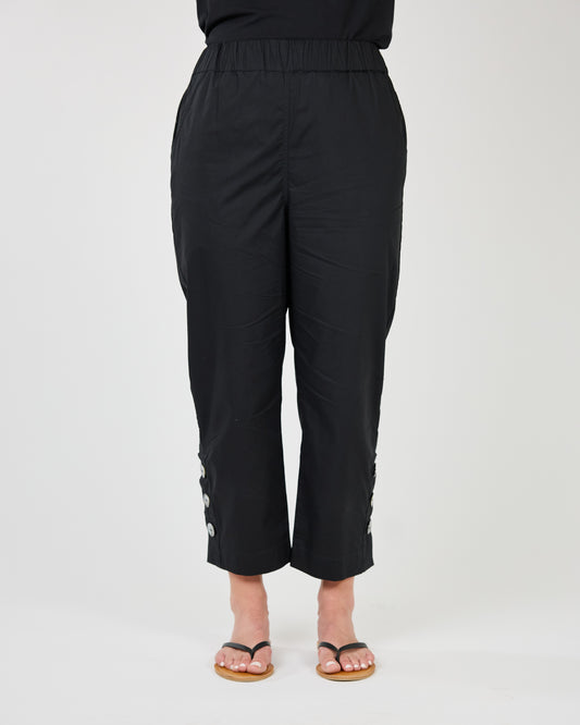 A person standing in black Shannon Passero Daisy Crop Pant with side button detailing and wearing brown sandals.