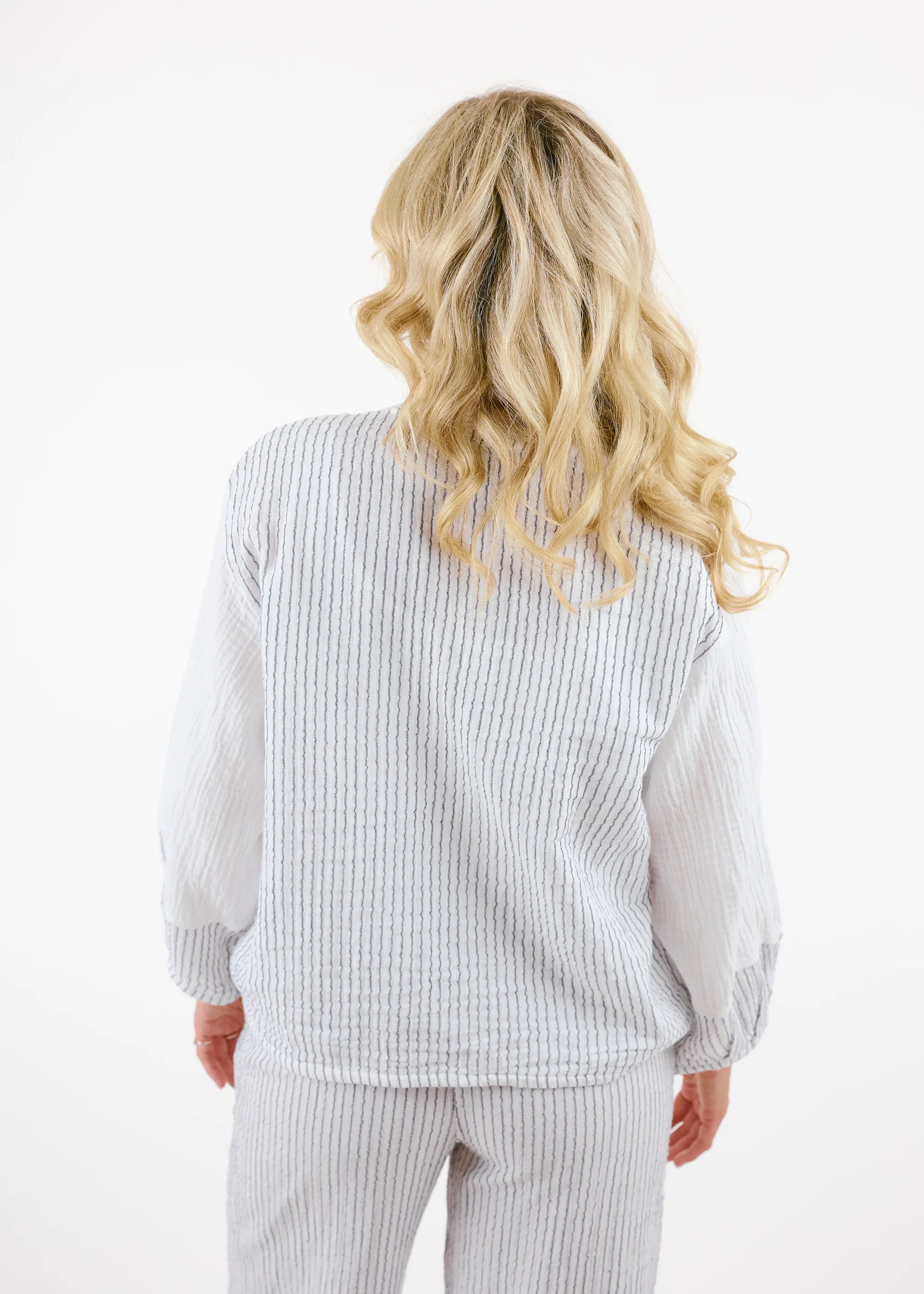 A woman with long blonde hair wears the Shannon Passero Kennedy Jlot—a white cotton gauze textured jacket with gray striped sleeves and matching pants—while standing against a plain white background.