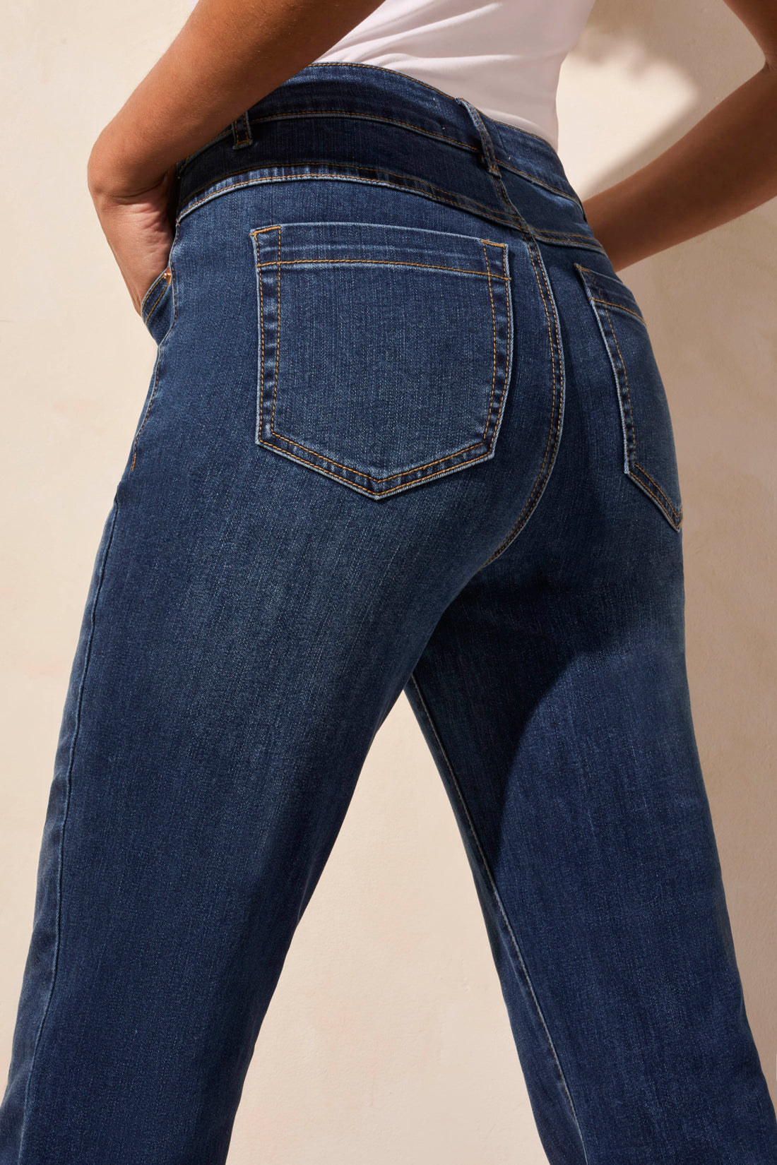 Wearing a white sleeveless top, the person stands against a light background in Tribal's AUDREY PULL-ON FLARE JEANS POCKETS.