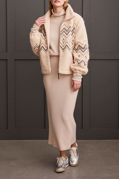 A person wearing a Tribal Lined Zip up Jacket with Embroidery in beige, paired with a matching ribbed dress, standing against a dark background.