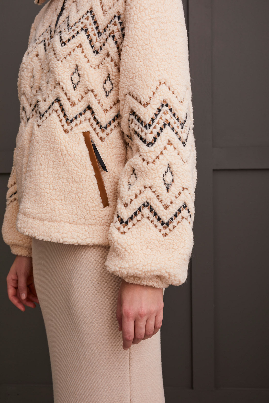 A person wearing a Tribal Lined Zip up Jacket with Embroidery in beige, paired with a matching ribbed dress, standing against a dark background.