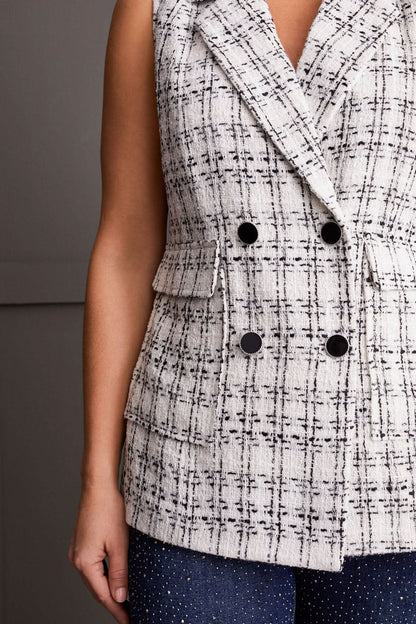 A person wearing the Tribal Lined Double Breast Sleeveless Tweed Vest, dark jeans with a sparkle pattern, and silver ankle boots stands in front of a paneled wall.