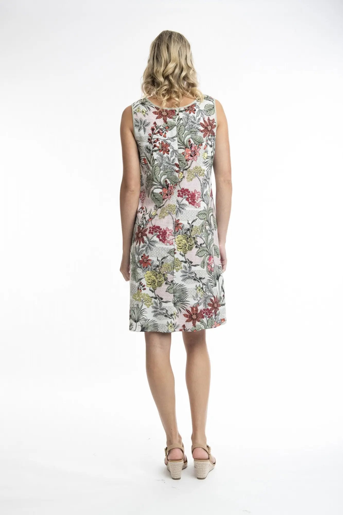 A woman stands smiling, wearing a Orientique Protaras 1 Dress Shift Sleeveless Reversible and beige heels against a white background.