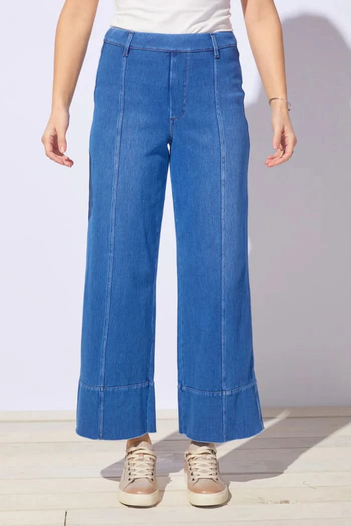 A person wears Escape’s Comfort Knit Denim Jean—high-waisted, wide-leg, and soft for everyday comfort—with beige sneakers, standing on a light floor against a white background.