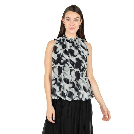A woman is shown from the back wearing the Black Flowing Petals Blouse by M Made In Italy, featuring a sleeveless design and a high neckline with a black and white floral pattern.