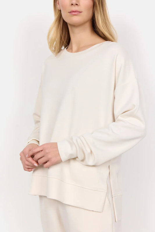 Wearing the Soya Concepts Banu Long Sleeve Sweater in off-white, paired with matching pants, this individual showcases relaxed style and all-day comfort against a simple backdrop.