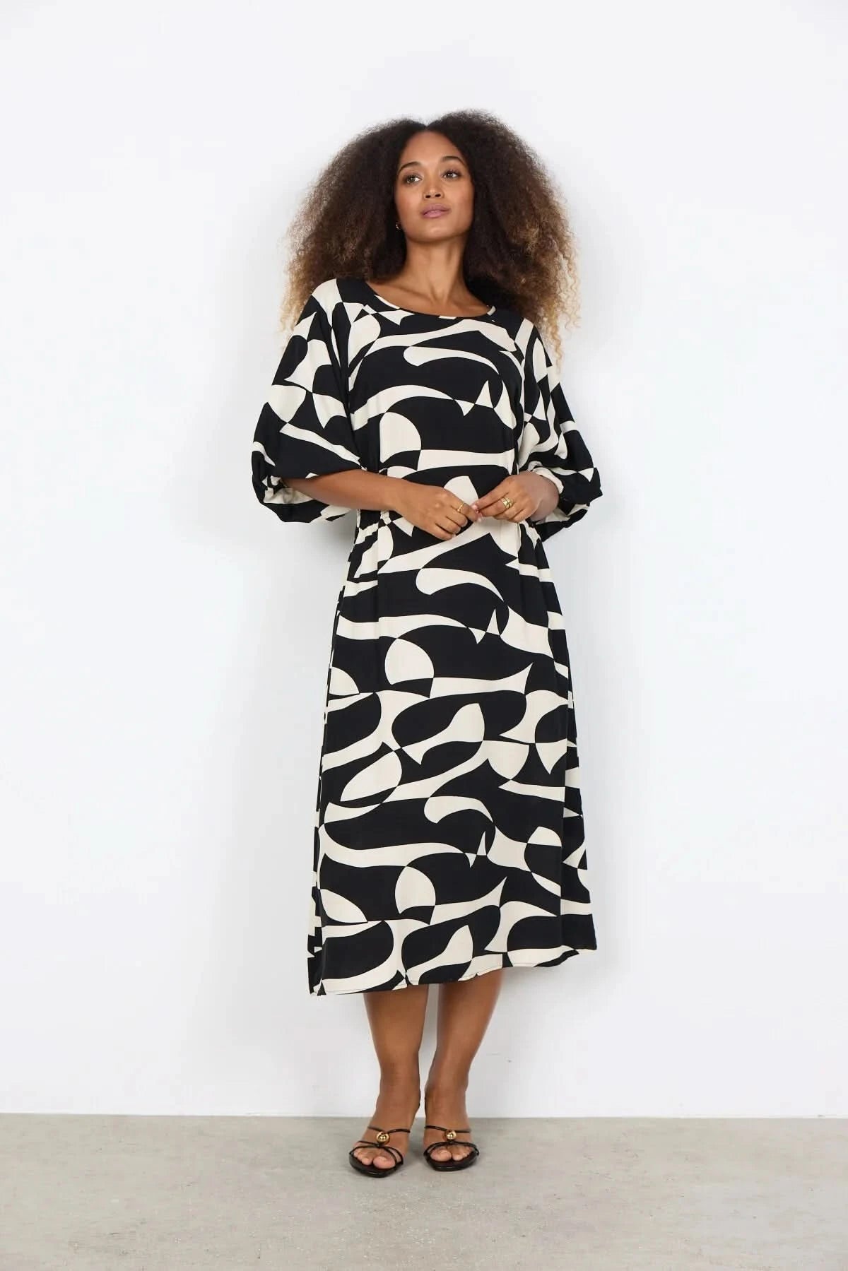 A woman wears the Chanise Dress by Soya Concepts, featuring a loose fit, black and white abstract print, and elbow-length sleeves, standing against a plain white background.