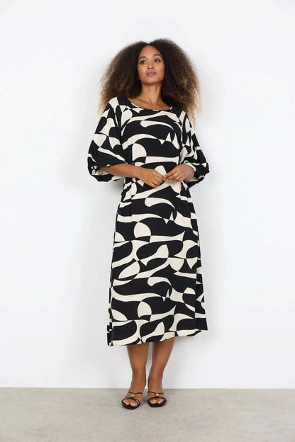 A woman wears the Chanise Dress by Soya Concepts, featuring a loose fit, black and white abstract print, and elbow-length sleeves, standing against a plain white background.