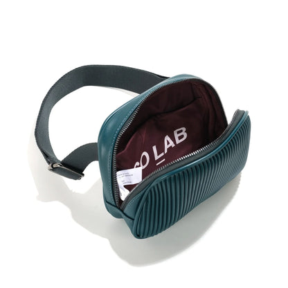 The Co-Lab Neoma sling bag features a small, rounded shape, teal vegan leather with a ribbed texture, and a wide black shoulder strap.