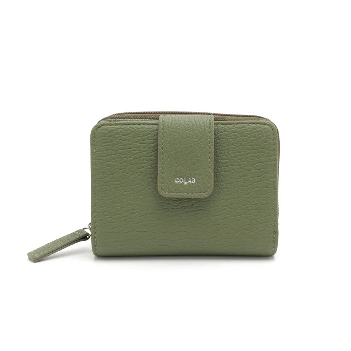 A person in a light gray shirt and beige pants holds The Lucie Small Wallet by Co-Lab, an eco-friendly, compact green wallet with both zipper and snap closures.