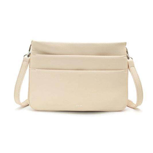 A person wearing a light gray blouse and beige pants carries Co-Lab’s The Nina Crossbody, an eco-friendly light green recycled vegan leather bag.