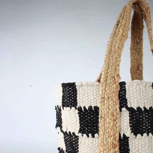The Co-Lab Laguna Beach Tote Bag showcases a chic black-and-white checkerboard pattern and a sturdy woven jute handle, standing upright against a plain background.