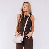 A woman in a sleeveless brown top and matching pants stands against a plain background, holding the Co-Lab THE 'MILA' SHOULDER BAG / CROSSBODY.