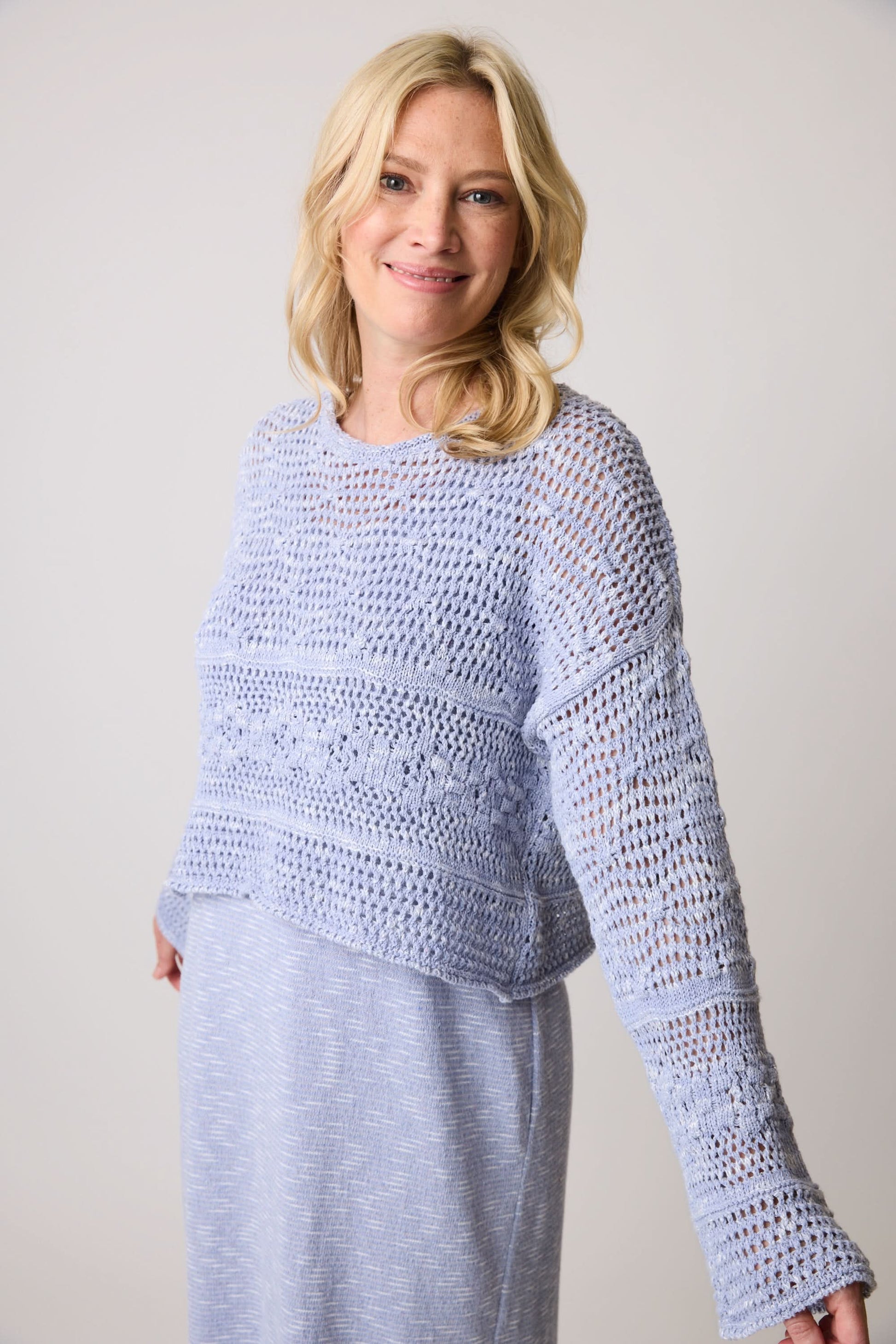 A woman with curly hair wears the Parkhurst Shorty Eco Shimmer Top in textured gray, looking to the side against a plain backdrop.