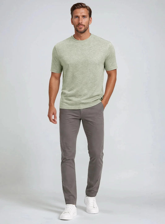 A man showcases effortless summer style in a Point Zero Mens Short Sleeve Active Top, paired with gray pants and white sneakers, standing against a plain background with one hand in his pocket.