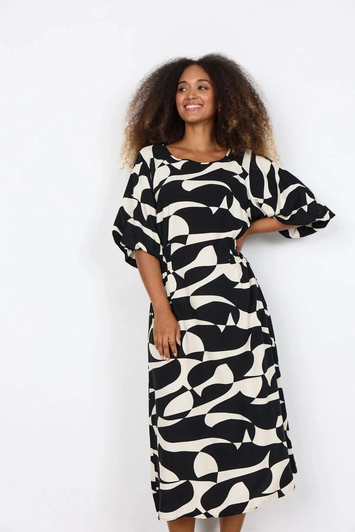 A woman wears the Chanise Dress by Soya Concepts, featuring a loose fit, black and white abstract print, and elbow-length sleeves, standing against a plain white background.