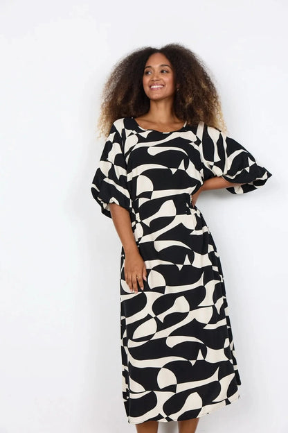 A woman wears the Chanise Dress by Soya Concepts, featuring a loose fit, black and white abstract print, and elbow-length sleeves, standing against a plain white background.