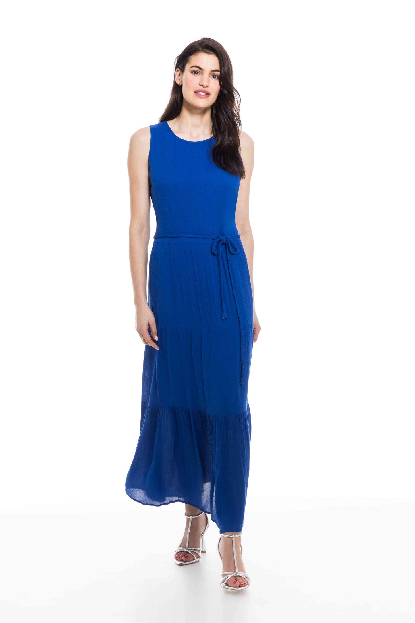A woman standing against a white background, wearing an Orly sleeveless front tie dress with a front tie at the waist and silver strappy heels.