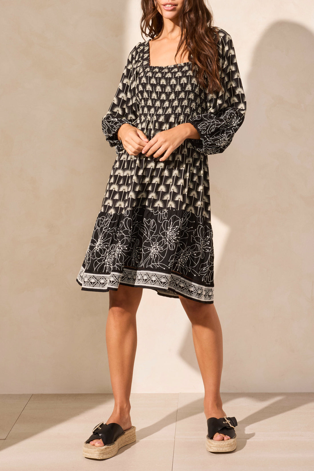 The woman confidently stands with hands on hips in a Tribal WEAR 2 WAYS EMBROIDERED DRESS, a versatile black and white patterned knee-length piece featuring long sleeves and a tie-front detail, paired perfectly with platform sandals.