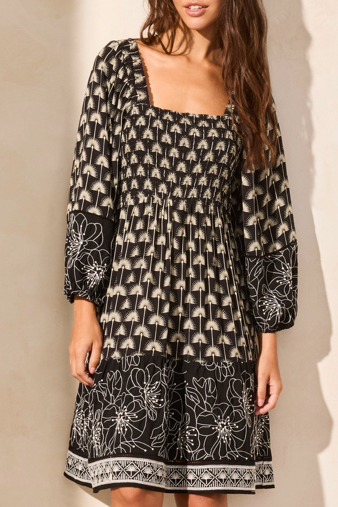 The woman confidently stands with hands on hips in a Tribal WEAR 2 WAYS EMBROIDERED DRESS, a versatile black and white patterned knee-length piece featuring long sleeves and a tie-front detail, paired perfectly with platform sandals.