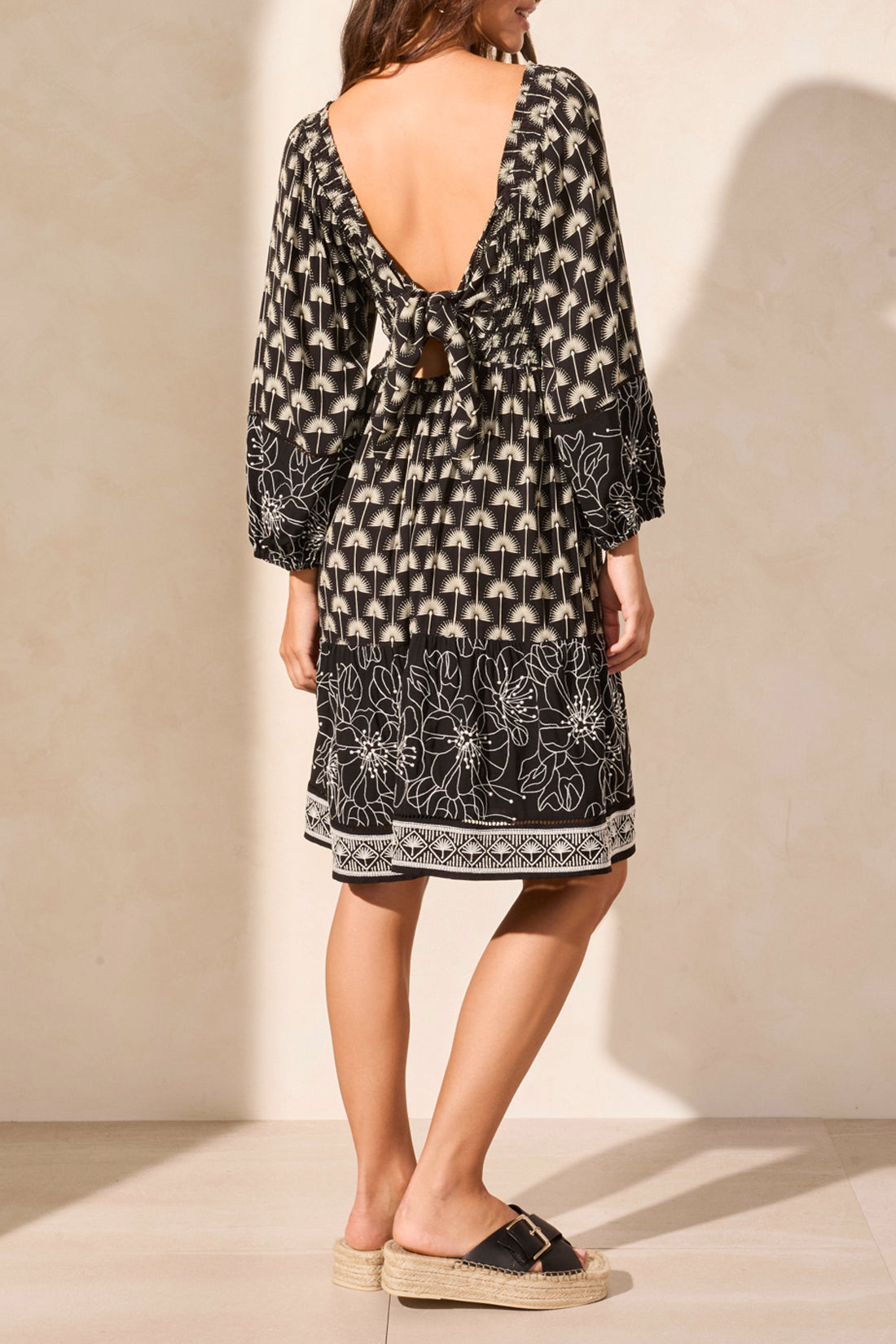 The woman confidently stands with hands on hips in a Tribal WEAR 2 WAYS EMBROIDERED DRESS, a versatile black and white patterned knee-length piece featuring long sleeves and a tie-front detail, paired perfectly with platform sandals.