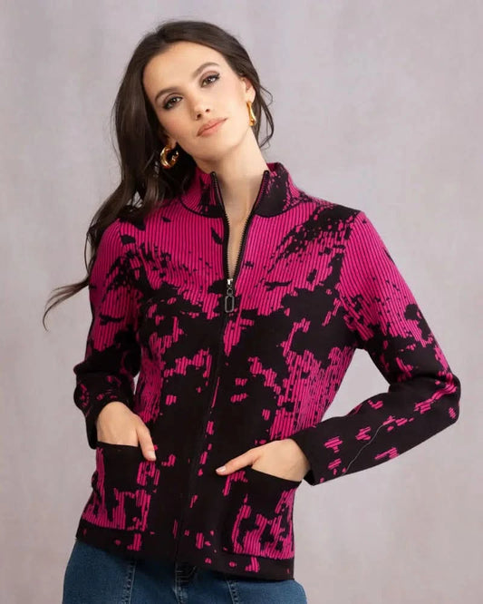 A woman wears the Alison Sheri Zip Up Knit Cardigan with a black and pink abstract pattern, hands in pockets, standing against a plain light background.