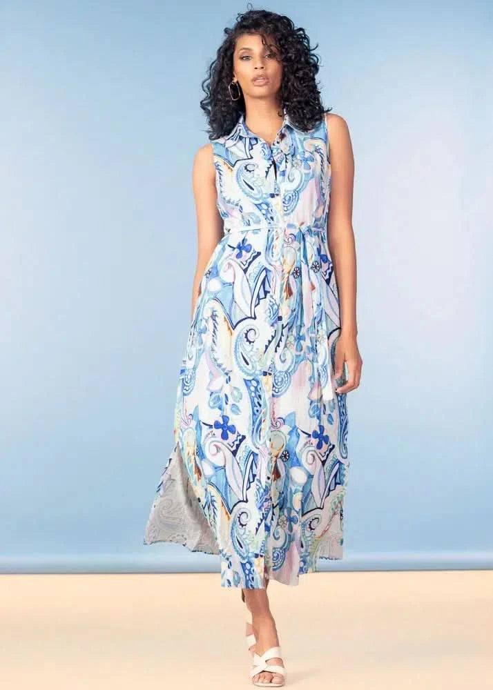 A woman models the Alison Sheri Midi Dress, featuring a sleeveless design, blue and white paisley pattern, and printed waist tie, set against a light blue background.