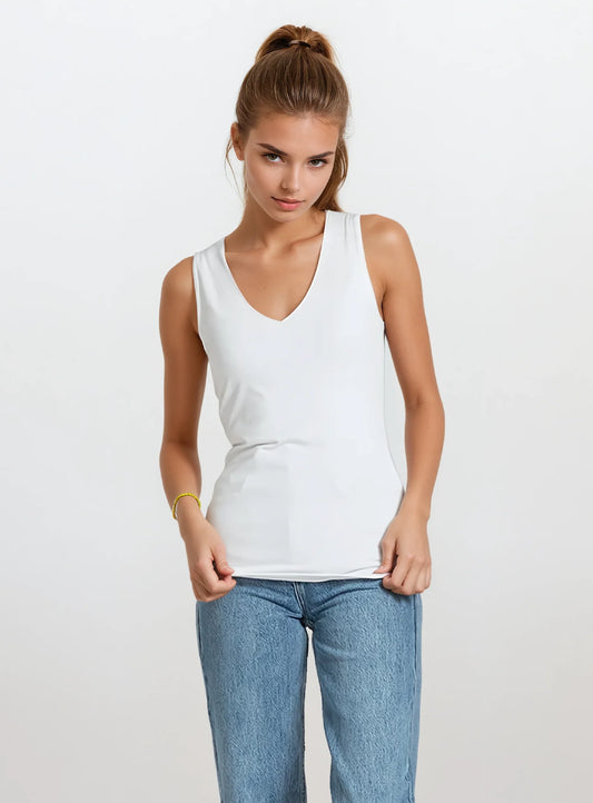 A woman wears the Point Zero Basic top, a sleeveless black V-neck tank, styled with a black skirt featuring white polka dots, standing against a plain white background.