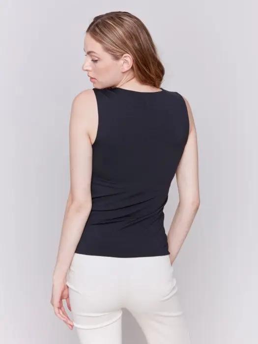 A person with long curly hair, wearing a Charlie B Super Stretch Sleeveless Top, blue jeans, and black ankle boots, stands posing against a plain background.