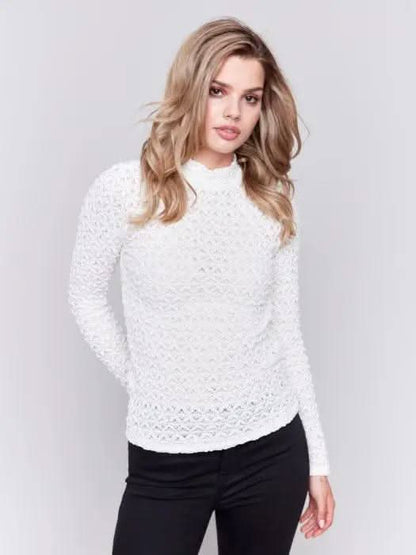 A woman with wavy blonde hair wearing a stylish Charlie B Basic Mock Neck Sweater and black pants stands against a light gray background.