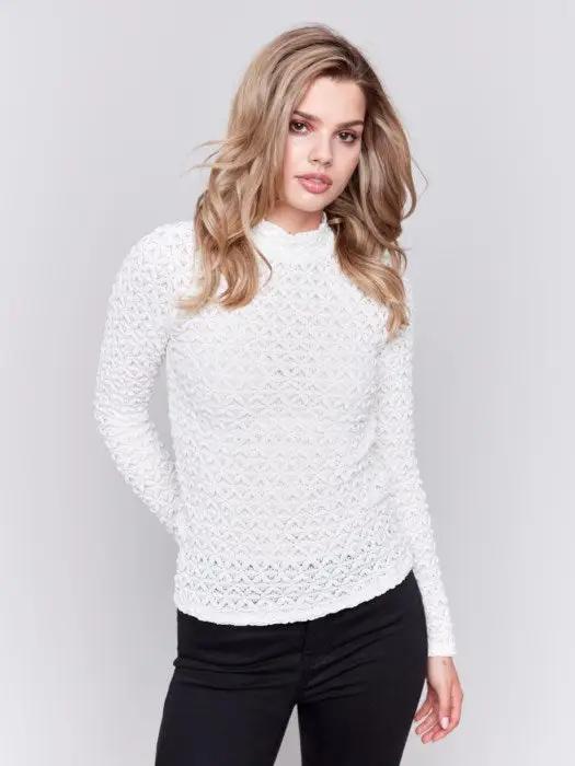 A woman with wavy blonde hair wearing a stylish Charlie B Basic Mock Neck Sweater and black pants stands against a light gray background.