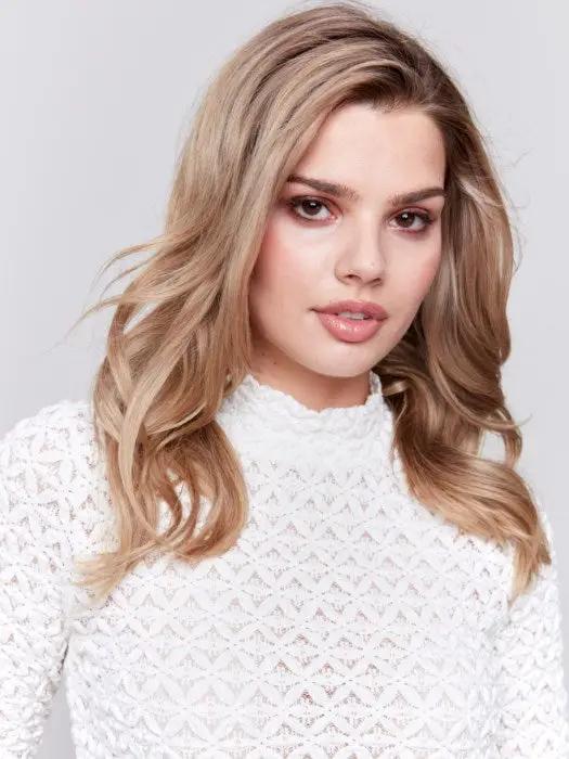 A woman with wavy blonde hair wearing a stylish Charlie B Basic Mock Neck Sweater and black pants stands against a light gray background.