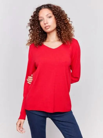 A person in a red Basic V Neck Long Sleeve Sweater by Charlie B and blue jeans stands against a plain background.