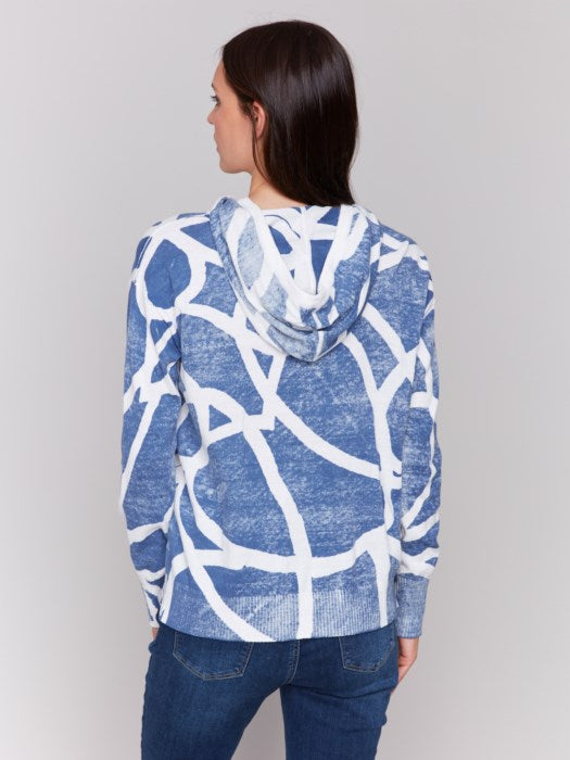 A person wearing the cozy and stylish Reverse Print Hoodie Sweater by Charlie B, featuring a blue and white pattern, pairs it with jeans against a plain gray background, exuding a playful print vibe.