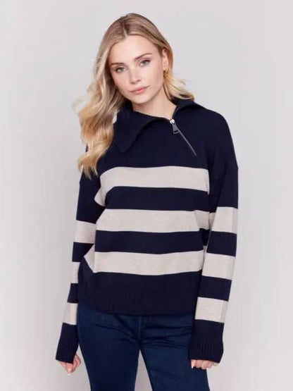 A person with light-colored hair wears a high-quality Charlie B Striped Turtleneck with Side Zip in navy and white, paired with dark pants against a plain background.
