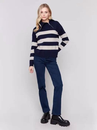 A person with light-colored hair wears a high-quality Charlie B Striped Turtleneck with Side Zip in navy and white, paired with dark pants against a plain background.
